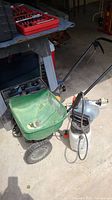 Green Scotts Turf Builder Edgeguard Mini Seed Spreader in garage setting with white garden sprayer attached.