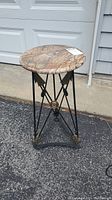 Full view of the round stone top side table with metal base against a driveway background.