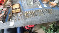 Wide view of multiple vintage spoons and forks laid out on cloth including boxed set in background.