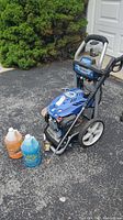 Full view of pressure washer with spray wand, hose and two cleaning solution jugs on driveway