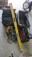 Photo showing two large soft tool bags, yellow spirit level, and Dewalt and blue corded power tools on the floor.
