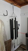 Full view of black metal wind chime hanging from hook against white wall