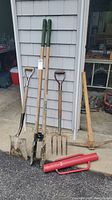 Full view of all yard tools including shovel, post hole diggers, pitch fork, pole hammer, and pick with a red handled tool in foreground