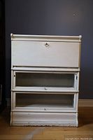 View of the closed antique white carriage writing desk with three glass-front lower storage compartments.