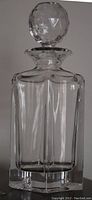 Clear geometric faceted glass whiskey decanter with stopper on top, shown from front.