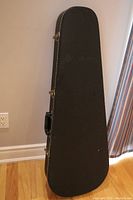 Closed view of black teardrop-shaped guitar case showing heavy duty vinyl exterior and metal clasps