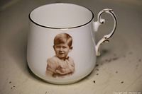 White bone china tea cup with gold rim and ornate handle, showing image of young King Charles on side