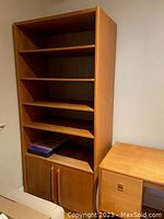 Tall teak bookcase with five shelves and two-door base cabinet, empty except for a few items on bottom shelf.