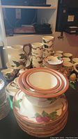 Stacked plates, cups, and pitcher displaying fruit and leaf decorative pattern with rustic rims