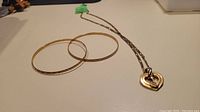 Two gold bangles and chain with pendant laid flat on white surface