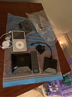 Apple iPod 160GB silver with charger cable, Altec Lansing speaker alarm clock unit, remote control, and power adapter on a cloth surface.