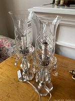 Two vintage glass lustres with tall cut glass hurricane shades and decorative crystal drop accents on a wooden table.