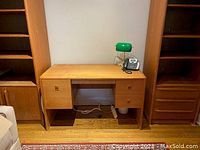 Full front view of Mid Century Modern teak desk showing four drawers and rounded side panels. Green lamp and phone on top with power strip underneath.