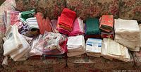 Wide view of many stacks of folded cloth napkins, table linens, and chicken motif napkin rings arranged on a floral couch