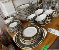 Photo showing stacked dinner plates, side plates, bread plates, cups, and one platter on a wooden table.