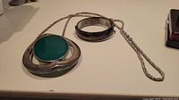 Photo showing large sterling necklace pendant with green stone and sterling chain, and the sterling engraved bangle bracelet.