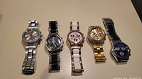 Full view of all 5 Swatch Irony watches arranged side by side, showing variety of colors and bands
