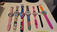 Seven different Swatch watches laid out in a row showing overall styling and band colors.