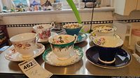 Full view of five teacups and saucers with detailed floral and gold accented designs.