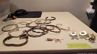 Overview of approximately 14 silver bangles and three pairs of earrings on a table surface