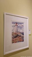 Framed lighthouse watercolour artwork hung on wall with a white frame and matting visible.