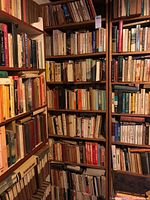 View of multiple wooden shelves filled densely with mixed collection of hardcover and paperback books of various sizes and colors