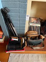 Photo showing tripod, camera bag, and darkroom processing trays on floor near vinyl records and books