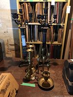 Overall view of brass candleholders and black metal multi-arm candelabras on wood table in front of shelves with various files