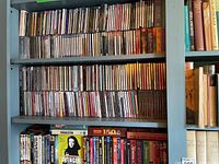 Three shelves of classical music CDs in plastic jewel cases on blue bookcase