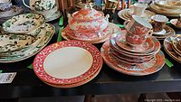 Full view of assorted china including Lenox Firesong plates, Arita Imari Peacock set, Royal Crown Derby Red Aves dinnerware on a table