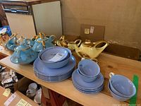 Overview of multiple china sets including blue teapots with gold trim, plates, and cream and sugar sets