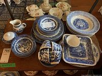 Assorted blue and white transferware pieces displayed on table showing dinner plates, bowls, cups, saucers, cream and sugar bowls, and serving pieces.