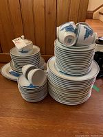 Multiple stacks of dinner plates, side plates, bowls, sugar bowl and creamer displayed on floor.