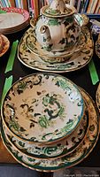 Photo shows Mason's Chartreuse pattern pedestal bowl on top of stack of plates, with teapot and underplate visible on black surface.