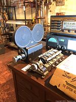 Front view showing Neumade Synchromaster film synchronizer with metal rollers and dials in foreground and Bach Auricon projector with twin reel arms behind.