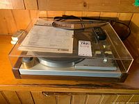 Overview of turntable with dust cover closed, manual, power cord and remote on top