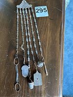 Full view of the antique metal chatelaine laid out on a wooden surface showing all chains and attached sewing tools