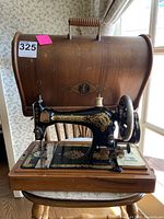 Antique Singer sewing machine with wooden base and closed wooden carrying case behind it
