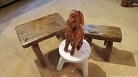 Three rustic antique wooden stools and one carved wooden dog figurine placed on a small white stool on carpeted floor
