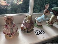 Photo showing mouse in pink plaid dress, frog sitting on log, rabbit in blue coat with white stockings, and part of another figurine