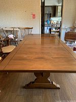 View of full length of rectangular wood dining table with leaf inserted, showing the table top and pedestal base.