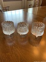 Three clear textured glass candle holders on wooden table showing melting ice pattern by Tapio Wirkkala for Iittala Ultima Thule series