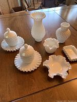 Photo of milk glass set on wooden table, showing full set of seven glass pieces including covered jam jars, vases, and candy dishes.