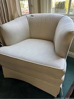 Front-right angle view of one cream tub chair showing curved back and skirted base