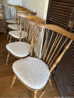Side view angle of five Vilas Windsor maple dining chairs arranged in a row on hardwood floor showing cushioned seat covers and back spindles