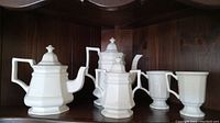 Complete set of white porcelain coffee pot, teapot, sugar bowl with lid, and two mugs on wood shelf.