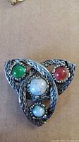Close-up front view of Celtic style Jacobite brooch with green, red, and light blue stones and metal Celtic knot design.