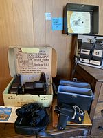 Vintage movie camera set with Kalart editor viewer, binoculars, Rolleicord camera in case, and film storage cases on display