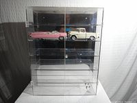 Front view of clear plexiglass display cabinet showing top two shelves with model cars and four empty shelves below, mirrored back visible.