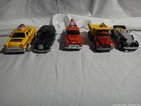 Front view of five diecast cars arranged side by side: New York taxi, London taxi, red truck, red dump truck, and red towing truck.